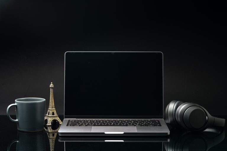 Laptop with black screen on working desk with cup and earphones on black background